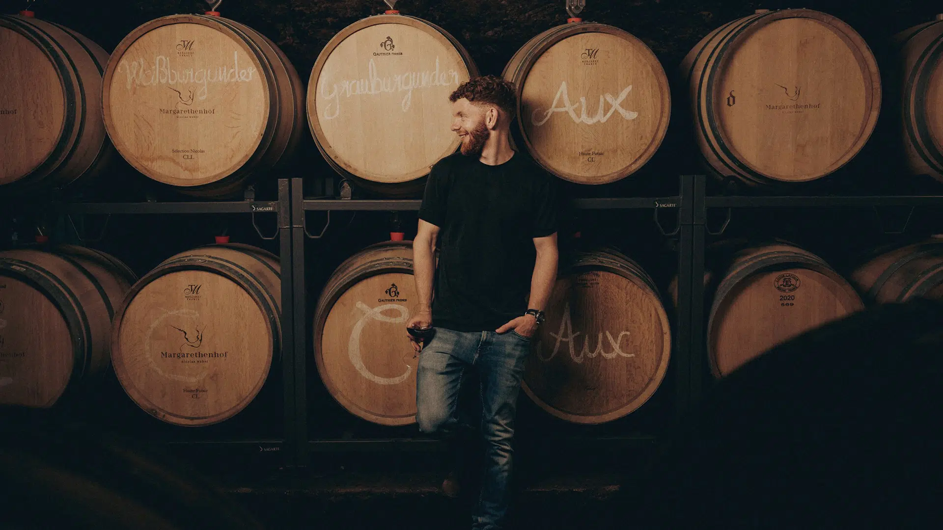 Nicolas Weber mit einem Glas Wein vor Holzfässern im Barriquekeller des Weinguts Margarethenhof